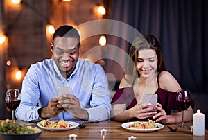 Phubbing. Young Interracial Couple Looking At Their Smartphones At Date In Restaurant photo