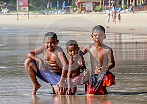 Local Asian children on the beach. Three boys playing in the waves.