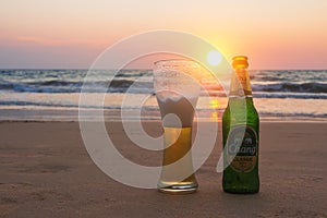 Phuket, Thailand - Mart 12, 2019: misted bottle and glass of cold Chang beer on the sand at the background of seascape, sunset sky