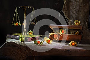 physalis fruits escape from a jewelery box to a brass scale, still life metaphor on a rustic wooden table in front of a dark