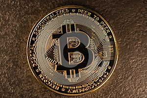 Physical Bitcoin coin in gold on metal surface. Blockchain symbol and cryptocurrency. Digital money transfer