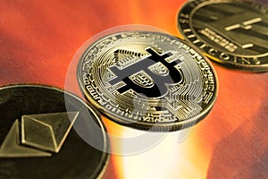 Physical Bitcoin, Litecoin and Ethereum gold coins with fire background