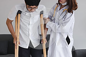 Physical female doctor helping patient with crutches in hospital office.