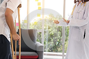 Physical female doctor helping patient with crutches in hospital office