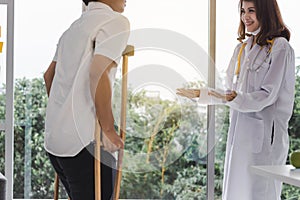 Physical female doctor helping patient with crutches in hospital office