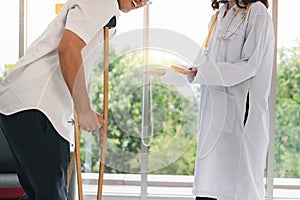 Physical female doctor helping patient with crutches in hospital office