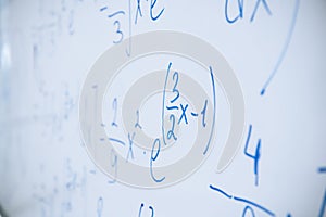 Physical and mathematical formulas written with a blue marker on a white board in a high school classroom. Abstract