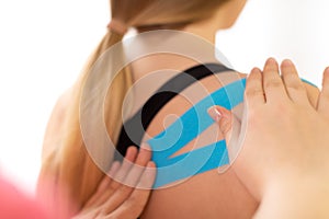 Physical therapist applying kinesio tape on female patient`s shoulder. Close up rear view. Kinesiology, physical therapy.