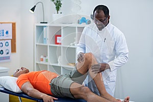 Physical therapist examining knee of sportsman lying near him