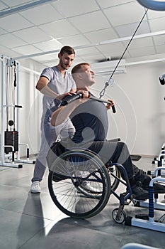 Physical therapist help wheelchair patient in gym. Man with paraplegia