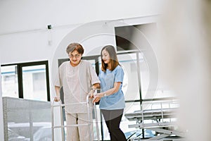 Physical therapist helping senior patient in using walker during rehabilitation