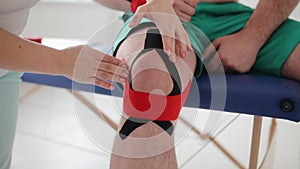 Physical therapist placing kinesio tape on male patients knee. Knee joint treatment. Sport and rehabilitation