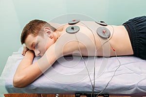 Physical therapist positioning electrodes for back muscle treatment young man