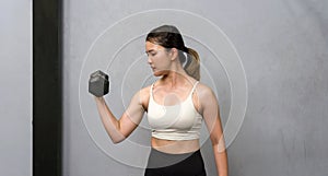 A physically fit woman engaged in a workout session at a modern gym, determinedly lifting a heavy dumbbell as she strives for