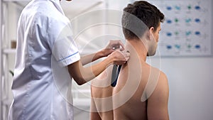 Physician applying Y-shaped tapes on patient upper back, reduce muscle tension