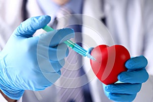 Physician arms wearing protective blue gloves stick needle into heart