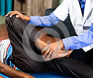 Physician exercising old man to stretch legs at home for joint pain relief - concept of senior people home health check