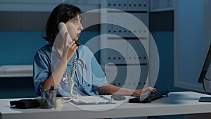 Physician nurse answering landline phone discussing patient report with remote doctor