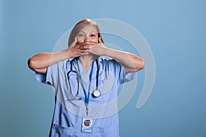 Physician nurse wearing medical uniform and stethoscope covering mouth with hand