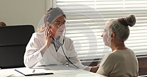 Physician using stethoscope listens sounds of heart of older patient