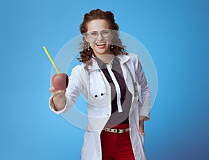 Physician woman giving apple with green cocktail tube on blue