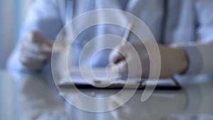 Physician writing prescription and holding pills, clinic, blurred background