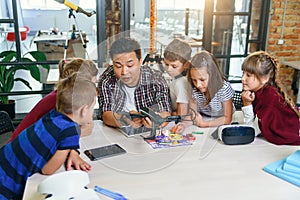 In physics and mechanics lesson young Asian teacher demonstrates quadcopter for caucasian pupils at class in modern