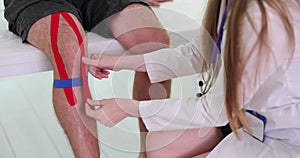 Physiotherapist applies kinesio tape to patient knee in clinic, closeup