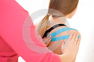 Physiotherapist applying kinesio tape on female patient`s shoulder and back. Kinesiology, physical therapy.