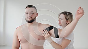 Physiotherapist Applying Kinesio Tape To Patients Injured Shoulder