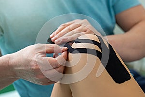 Physiotherapist applying kinesiology tape to patient knee.