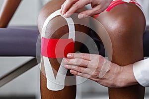 Physiotherapist applying kinesiology tape to patient knee.Therapist treating young female African American athlete