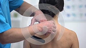 Physiotherapist applying Y-shaped tapes on female patient shoulder muscle strain
