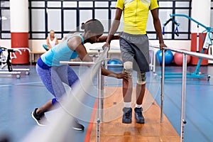 Physiotherapist assisting disabled man walk with parallel bars in sports center