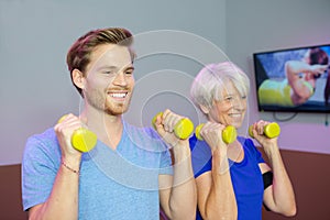 Physiotherapist assisting female senior to lift dumbbell