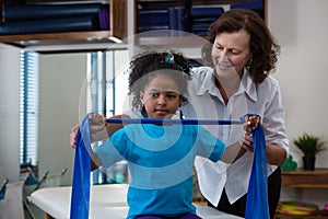 Physiotherapist assisting girl patient in performing stretching exercise from resistance band