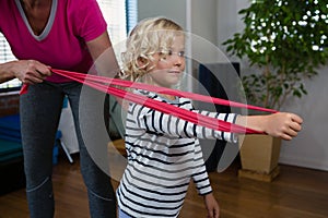 Physiotherapist assisting girl patient in performing stretching exercise with resistance band