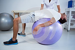 Physiotherapist assisting man with exercise ball