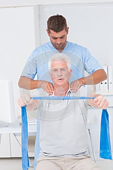 Physiotherapist assisting senior man in exercising with resistance band