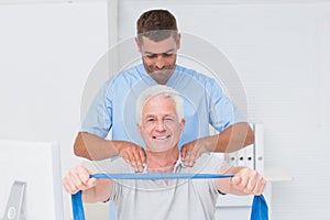 Physiotherapist assisting senior patient in exercising with resistance band