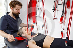 Physiotherapist assists female patient undergoing rehabilitative physiotherapy on a suspension rope system.