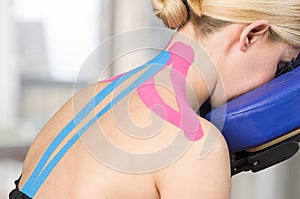 Physiotherapist, chiropractor putting on pink kinesio tape on woman patient. Pink: cervical, trapezius, supraspinatus, blue: high