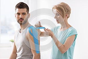 Physiotherapist covering selected fragments of young man`s body with special structure patches during kinesiotaping therapy photo