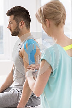 Physiotherapist covering selected fragments of young man`s body with special structure patches during kinesiotaping therapy