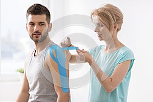 Physiotherapist covering selected fragments of young man`s body with special structure patches during kinesiotaping therapy