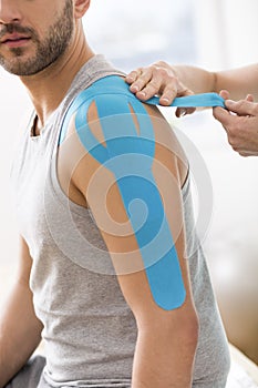 Physiotherapist covering selected fragments of man`s body with special structure patches during kinesiotaping therapy photo