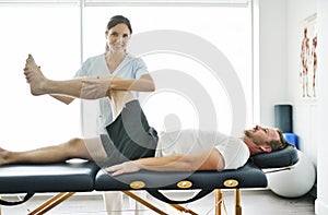 Physiotherapist doing treatment with patient in bright office with leg training