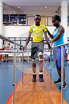 Physiotherapist helping disabled man walk with parallel bars in sports center