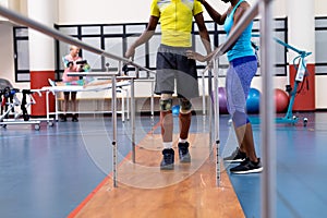 Physiotherapist helping disabled man walk with parallel bars in sports center