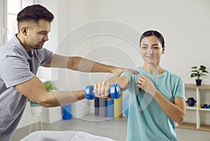 Physiotherapist helping patient to do muscle rehabilitation exercises with dumbbells